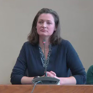 Woman seated in front of microphone provides testimony